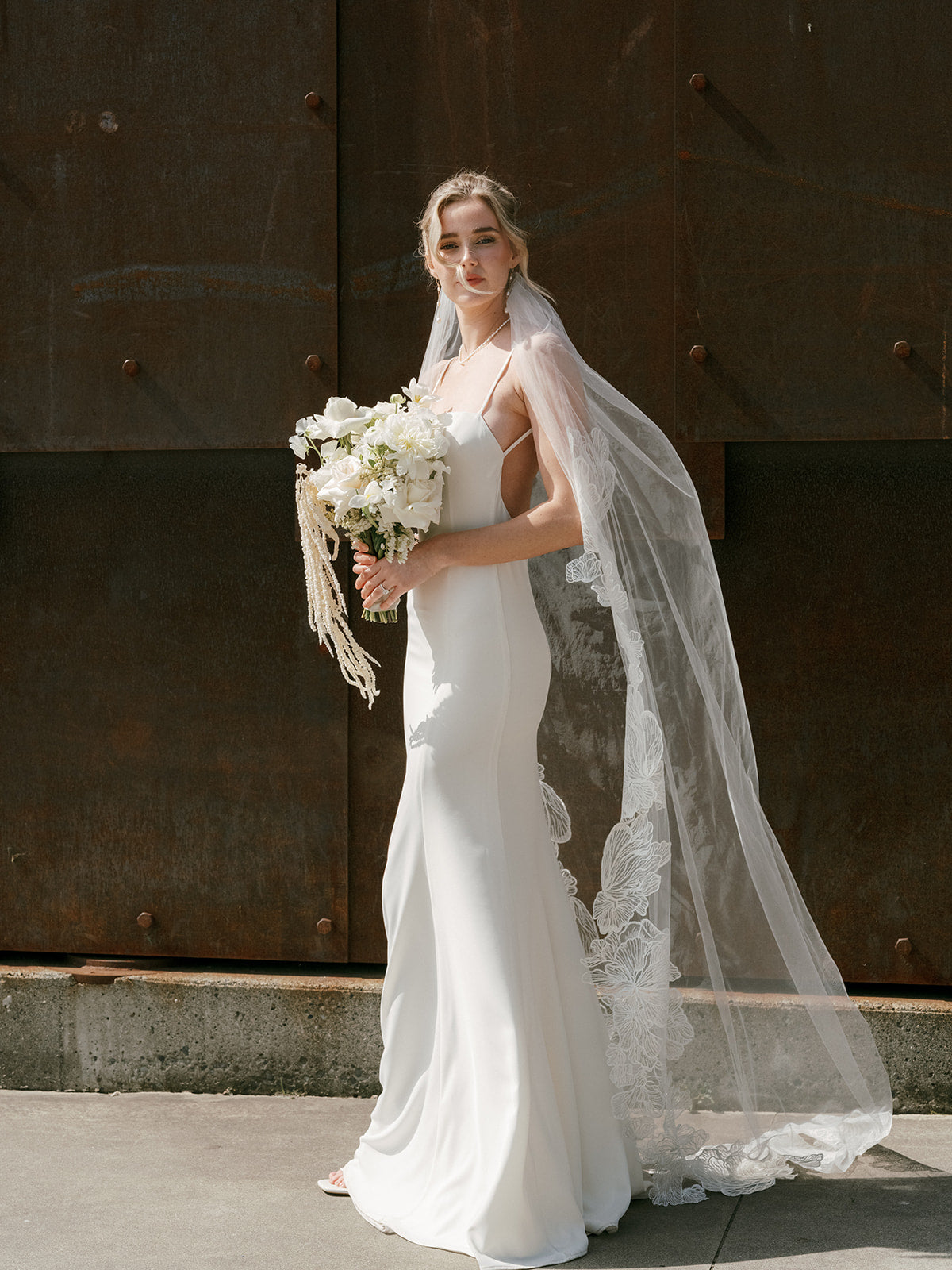 Bride in a wedding dress and cathedral wedding veil hold a floral bouquet