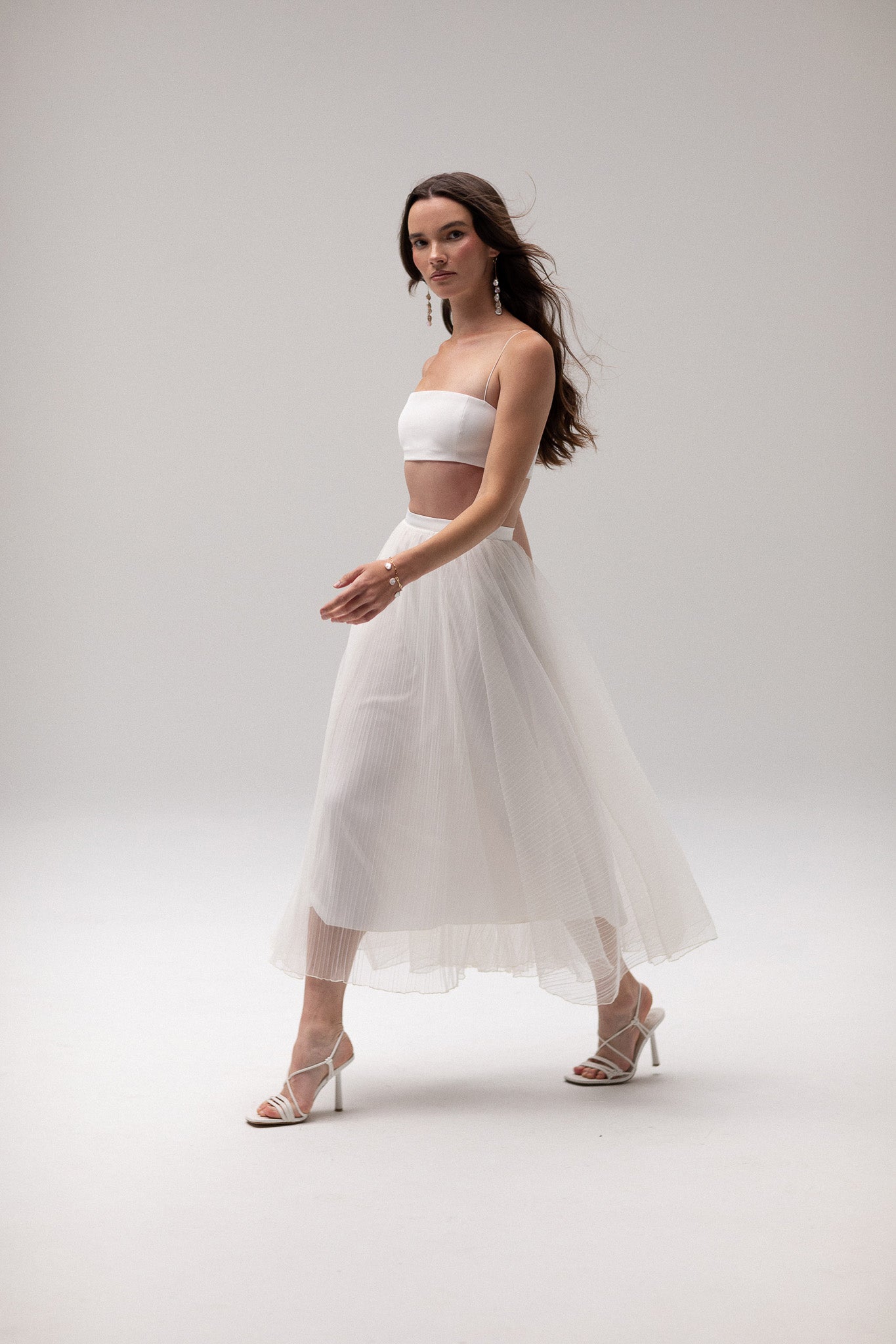 Model wearing a pleated tulle skirt overlay from the J'OSE Collection by TEMPÊTE, featuring a sheer, flowing design perfect for layering over bridal outfits.