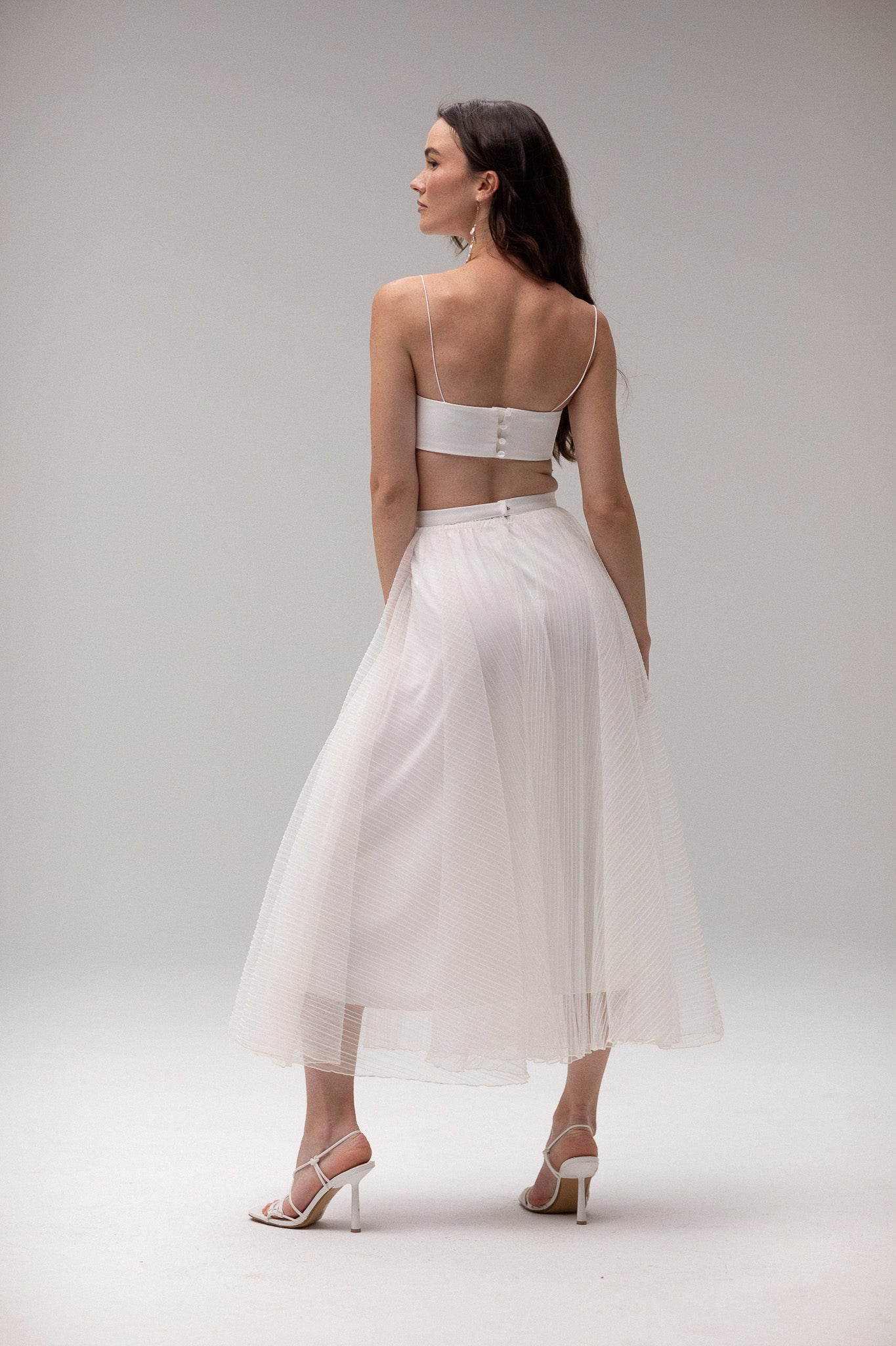 Model wearing a pleated tulle skirt overlay from the J'OSE Collection by TEMPÊTE, featuring a sheer, flowing design perfect for layering over bridal outfits.