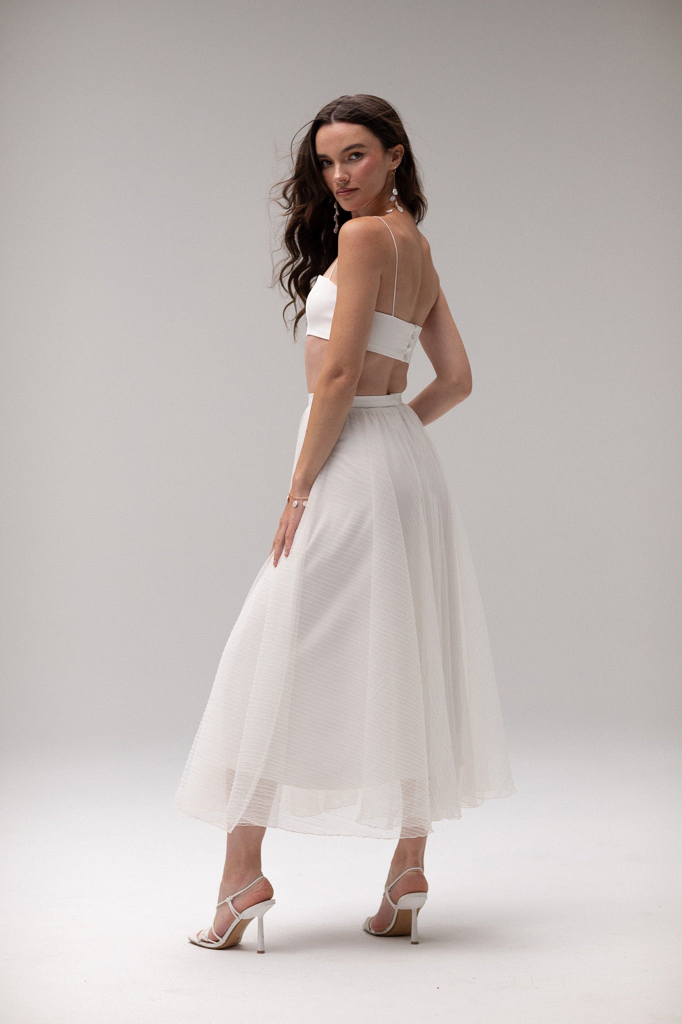 Model wearing a pleated tulle skirt overlay from the J'OSE Collection by TEMPÊTE, featuring a sheer, flowing design perfect for layering over bridal outfits.