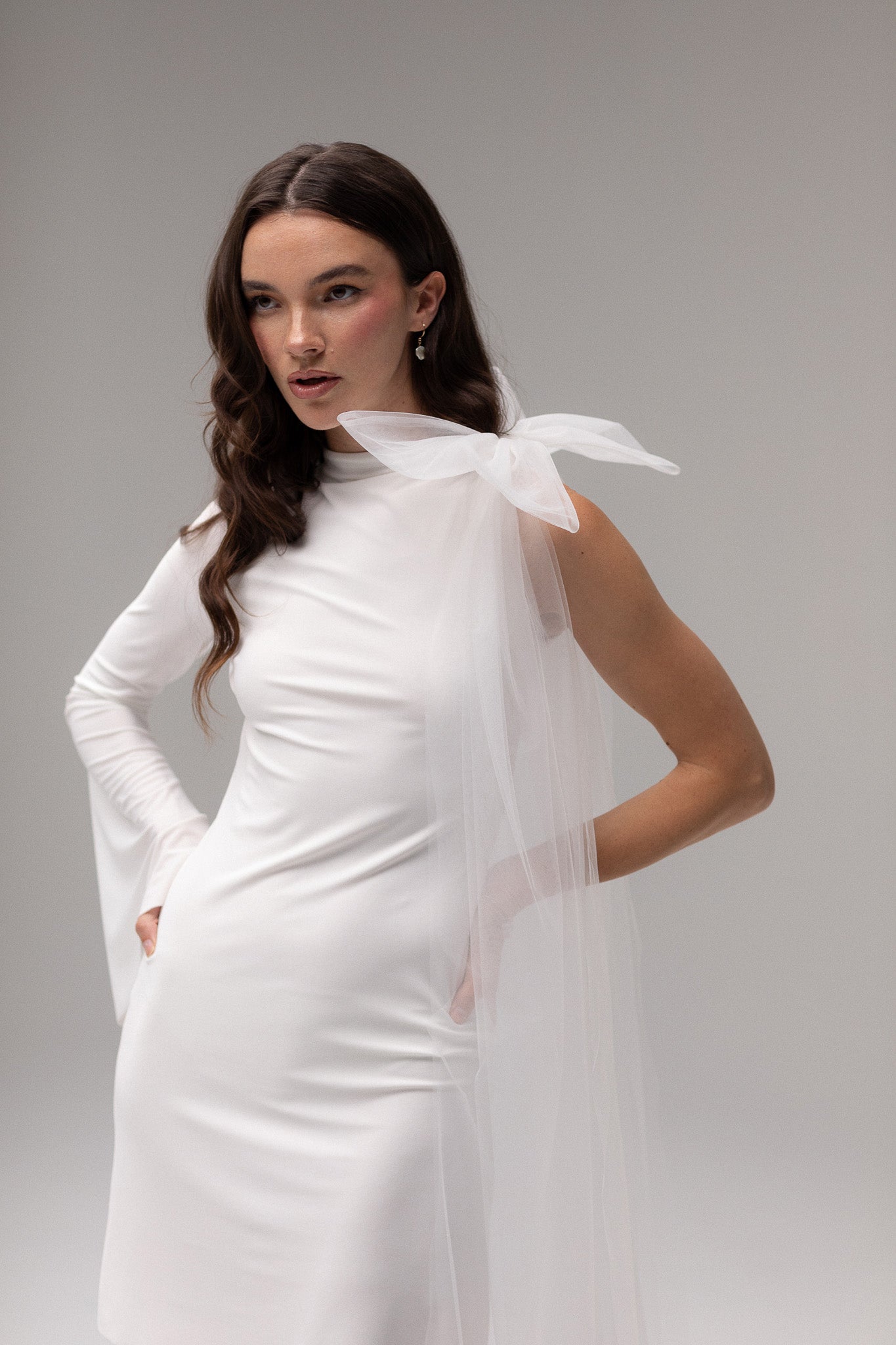 Model wearing a one-sleeve knit dress from the J'OSE Collection by TEMPÊTE, featuring a sleek silhouette and modern, asymmetric design for a bold bridal look.