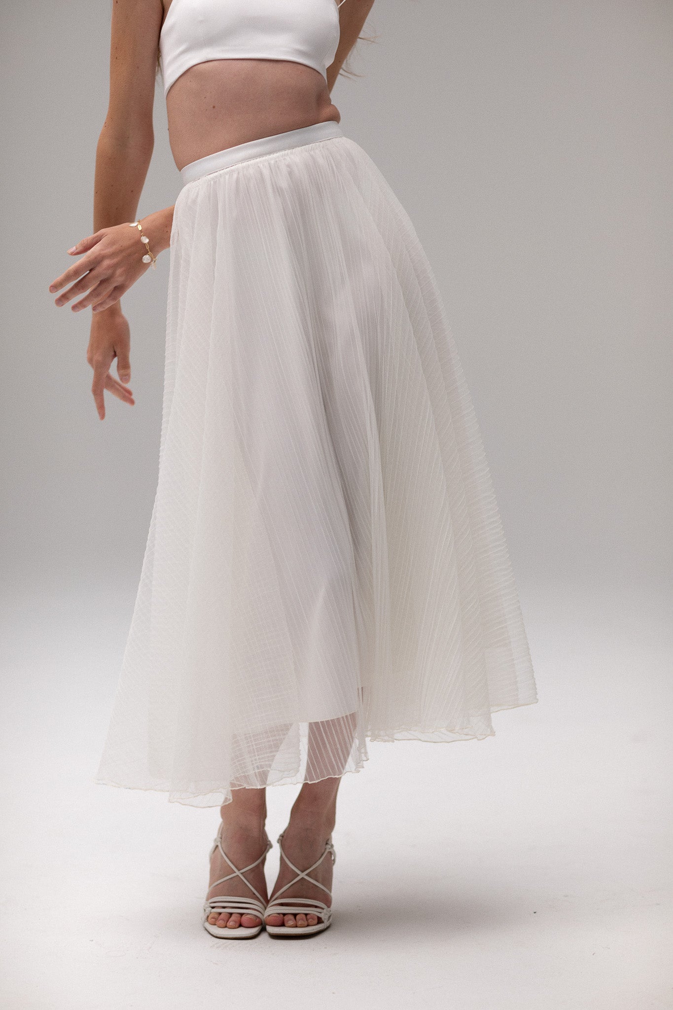 Model wearing a pleated tulle skirt overlay from the J'OSE Collection by TEMPÊTE, featuring a sheer, flowing design perfect for layering over bridal outfits.