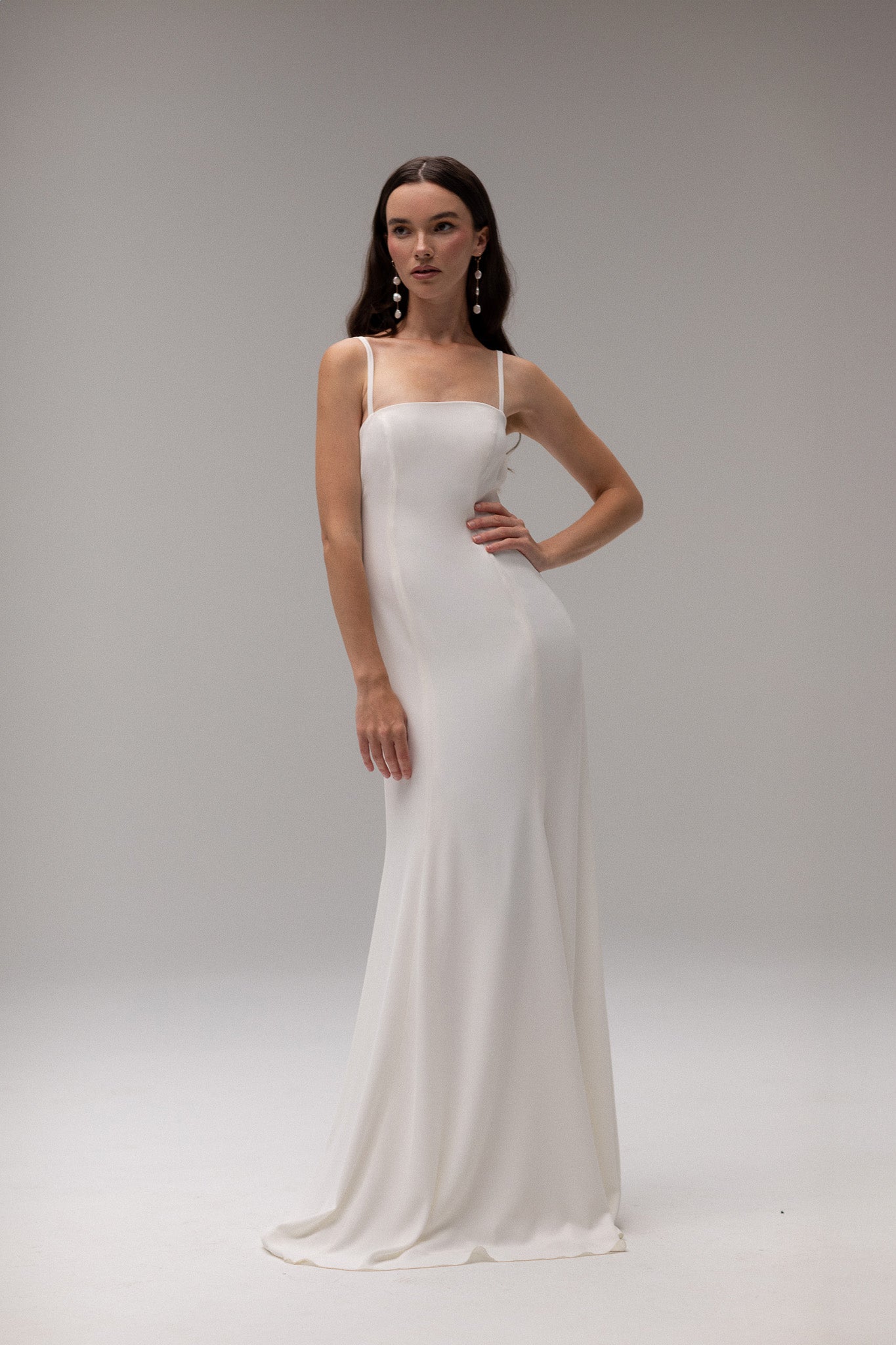 Model wearing an open back crepe gown from TEMPÊTE, featuring a voluminous skirt and square neckline for a sophisticated bridal look.