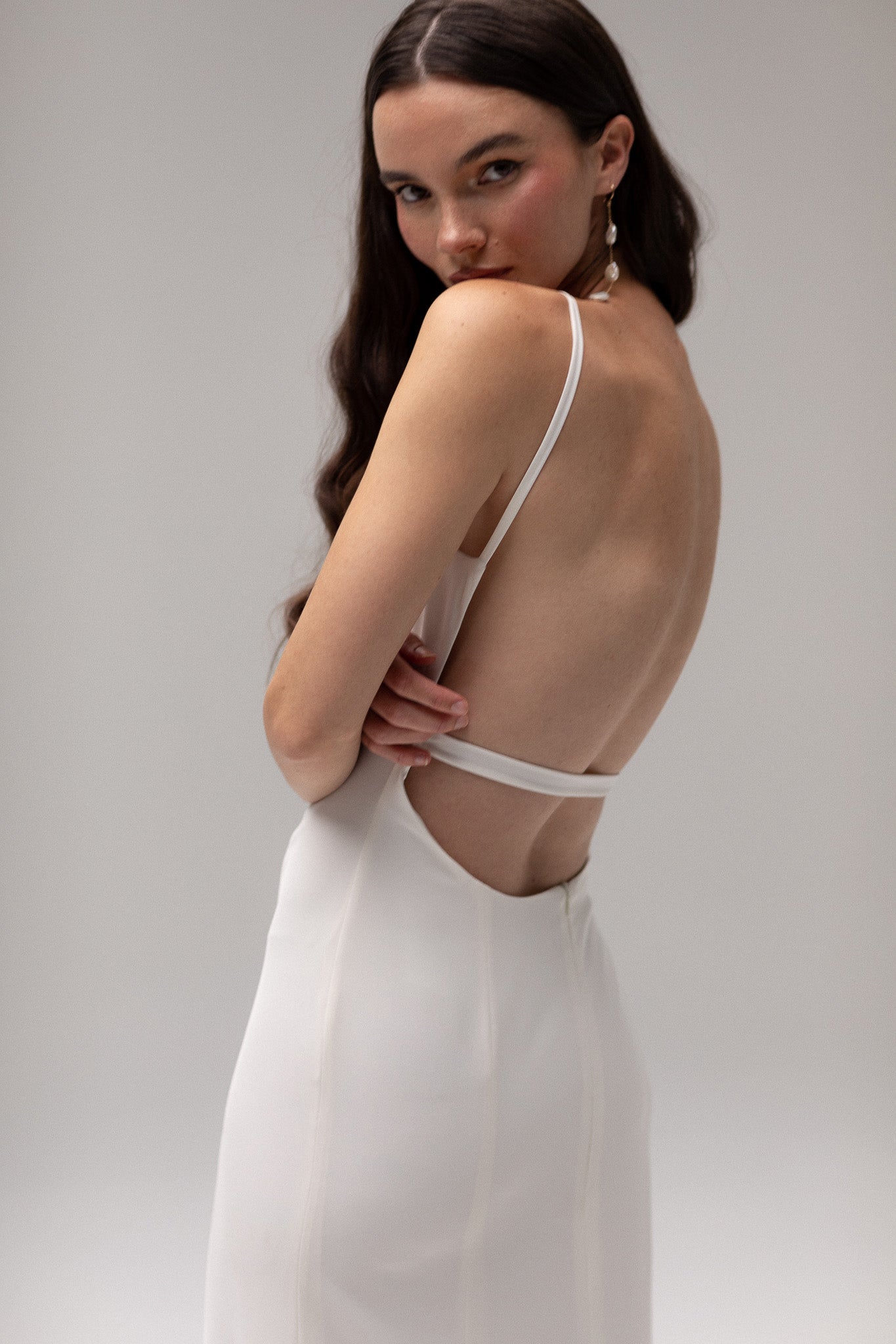 Model wearing an open back crepe gown from TEMPÊTE, featuring a voluminous skirt and square neckline for a sophisticated bridal look.