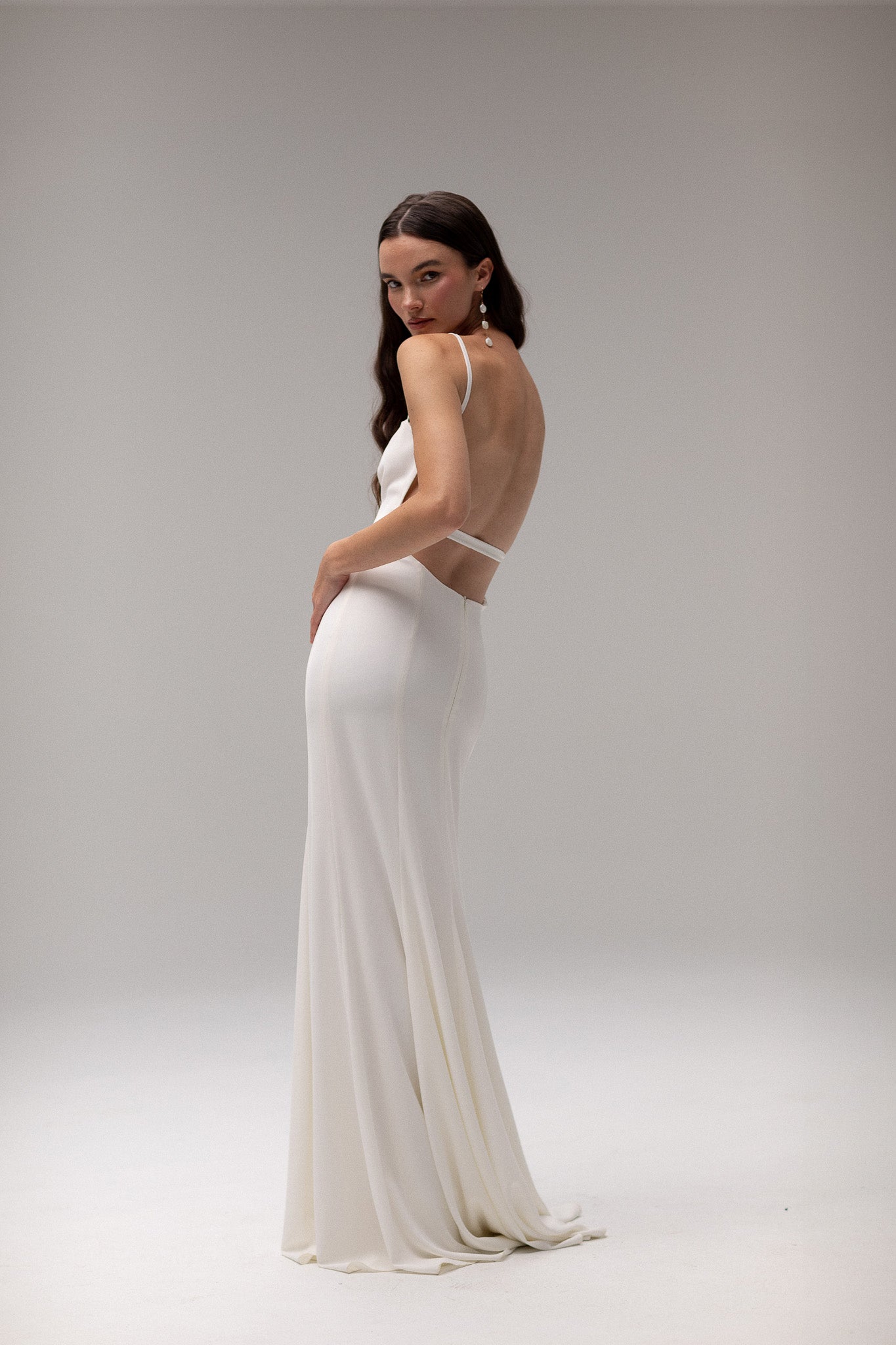 Model wearing an open back crepe gown from TEMPÊTE, featuring a voluminous skirt and square neckline for a sophisticated bridal look.